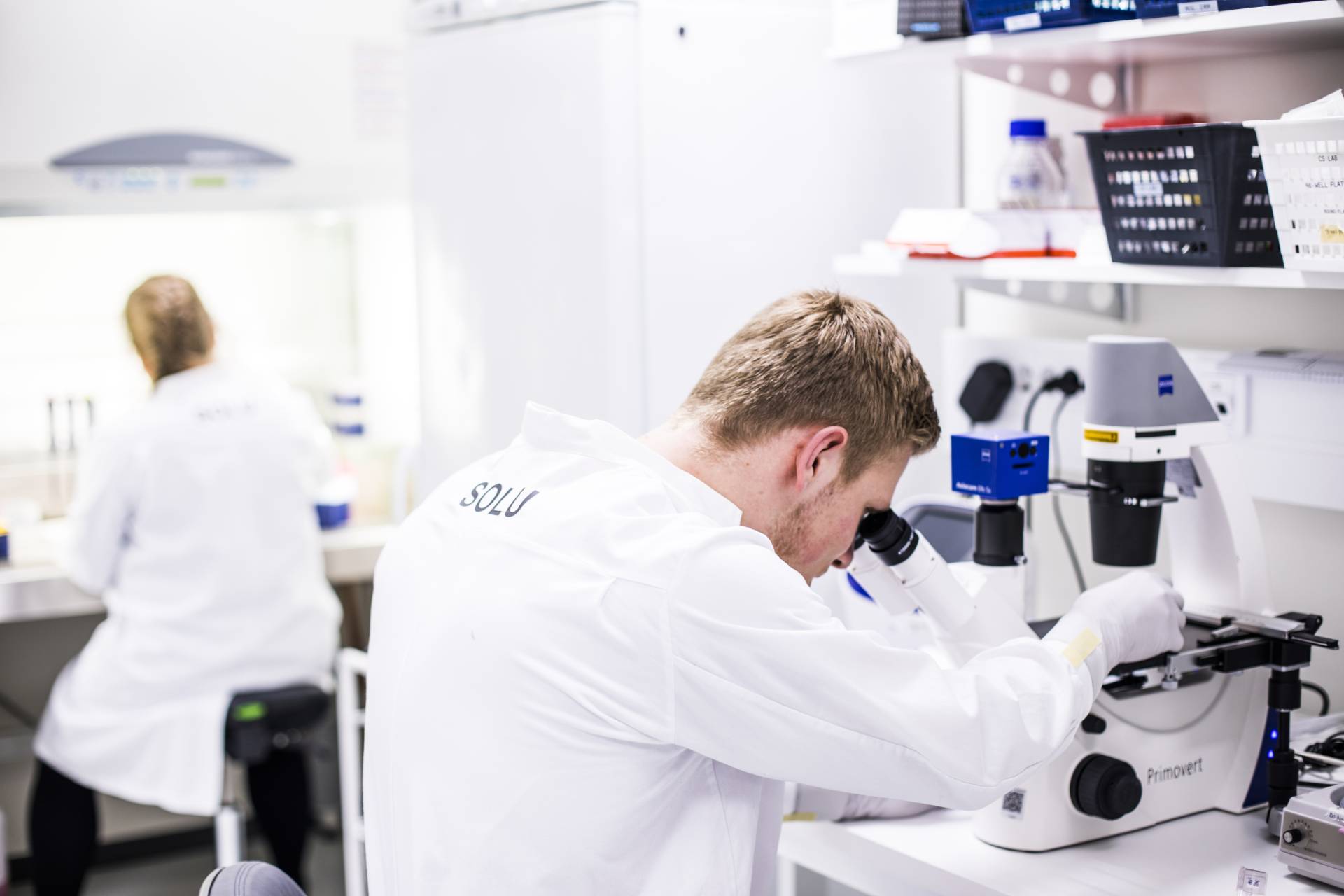 syöpälaboratorio, kaksi tutkitjaa, toinen mikroskoopin ääressä.